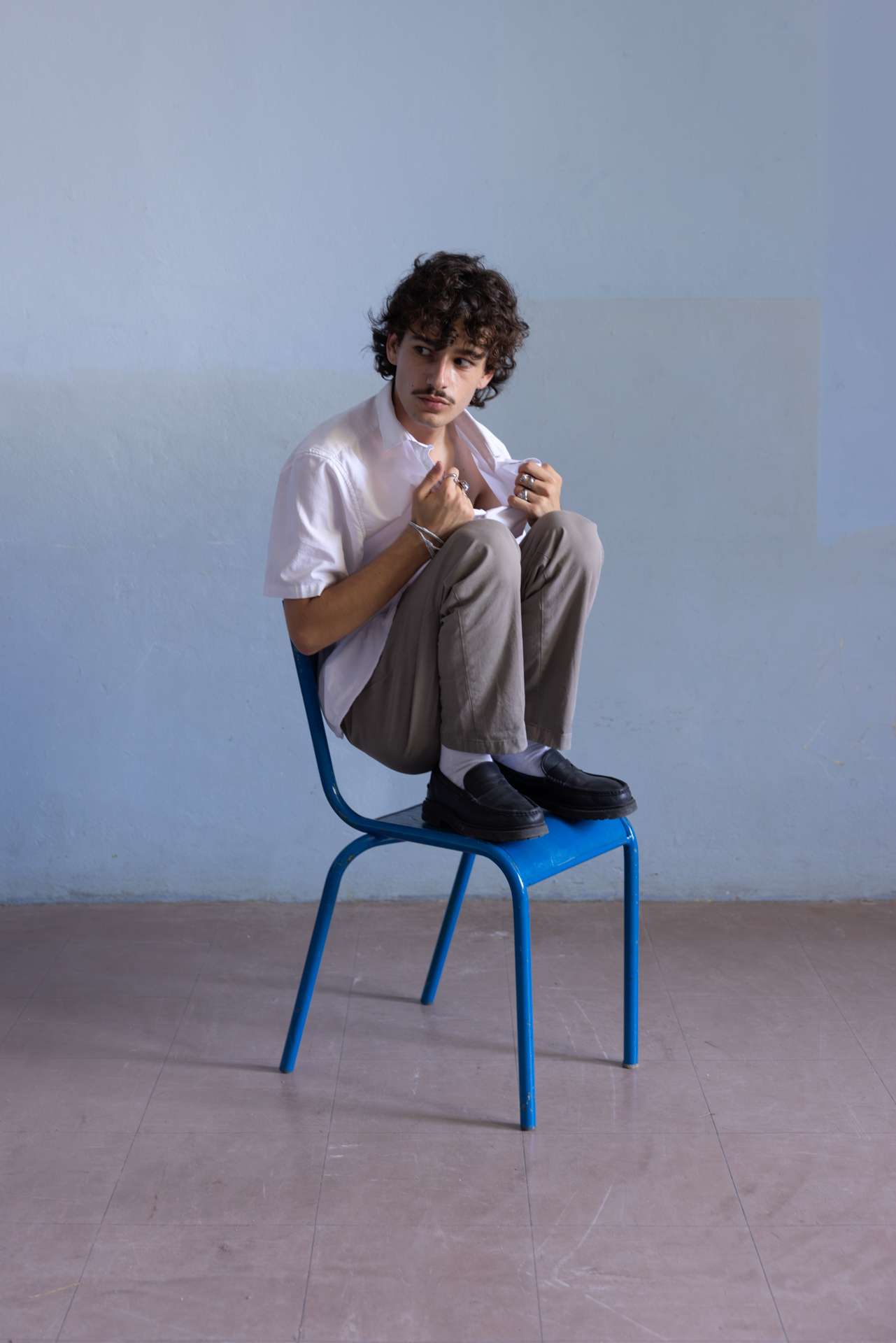 Photo d'un homme assis sur une chaise, en train d'arracher sa chemise, le regard de côté.